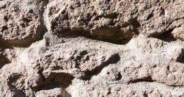 Kaba bir dokusu olan taştan yapılmış bir duvar. Duvar kahverengi ve bir sürü çıkıntısı ve çıkıntısı var.