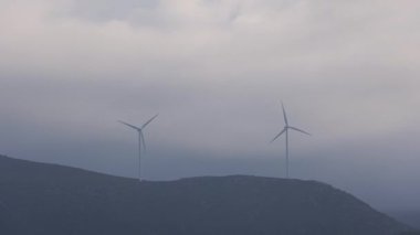 Fırtınanın ortasında bir çiftlikte duran iki rüzgar türbininin hızlanması. Kara bulutlar atmosferi döndürürken..