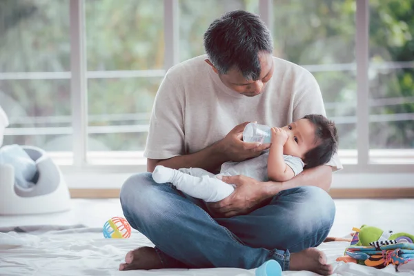 Asyalı baba kucağında bebeğini süt şişesiyle besliyor..