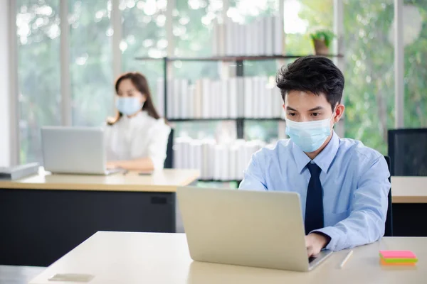 Asian business people with medical mask for virus protection working in office. new normal and social distancing concept.