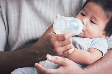 Asyalı baba kucağında bebeğini süt şişesiyle besliyor..
