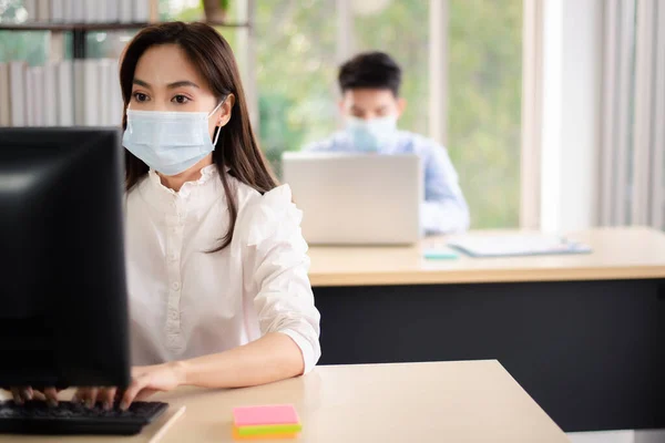 Asian business people with medical mask for virus protection working in office. new normal and social distancing concept.