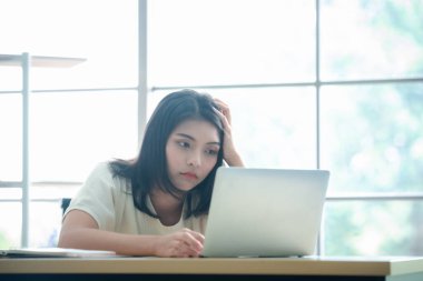 Dizüstü bilgisayar kullanan stresli genç Asyalı kadın, işten dolayı yorgun.