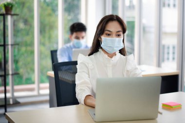 Virüs koruması için tıbbi maskeli Asyalı iş adamları ofiste çalışıyor. yeni normal ve sosyal uzaklık kavramı.