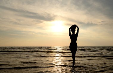 Baltık Denizinde günbatımı bir arka plan üzerinde genç bir kadın silüeti.