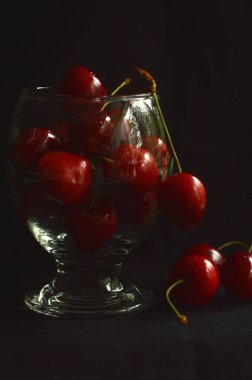 Olgun, koyu bir arka plan karşı cam kadeh tatlı bir kiraz kırmızı çilek.