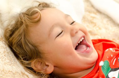 Küçük çocuk yatakta gülüyor.