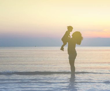 Gün batımında sahilde anne ve bebek siluetleri