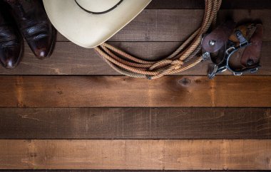 American Cowboy Items incluing a lasso spurs and a traditional straw hat on a wood plank background clipart