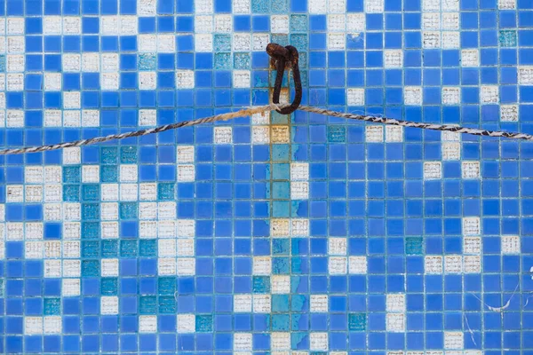 Rusty metal hook in turquoise tile wall in pool. Tile fell off in places and needs repair. Grunge texture. Restoration.