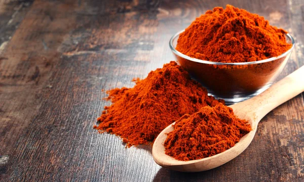 Composition with bowl of chili powder on wooden table.