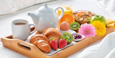 Otel odasında yatakta kahvaltı tepsisi. 