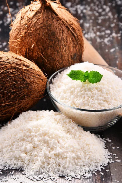 Composition with bowl of shredded coconut and shells on wooden table