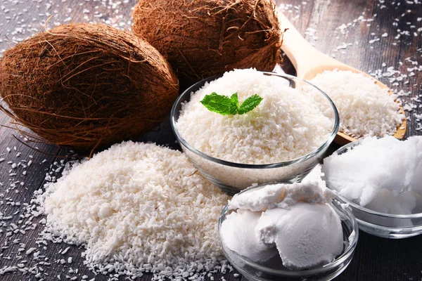 Composition with bowl of shredded coconut and shells on wooden table