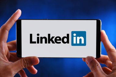 Linkedin logosunu gösteren akıllı telefonu tutan eller
