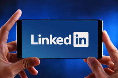 Linkedin logosunu gösteren akıllı telefonu tutan eller