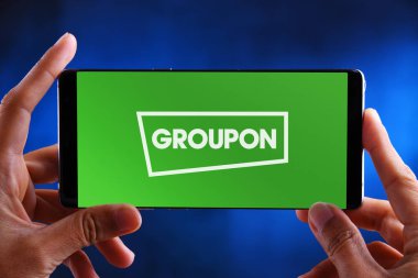 Groupon logosunu gösteren akıllı telefonu tutan eller