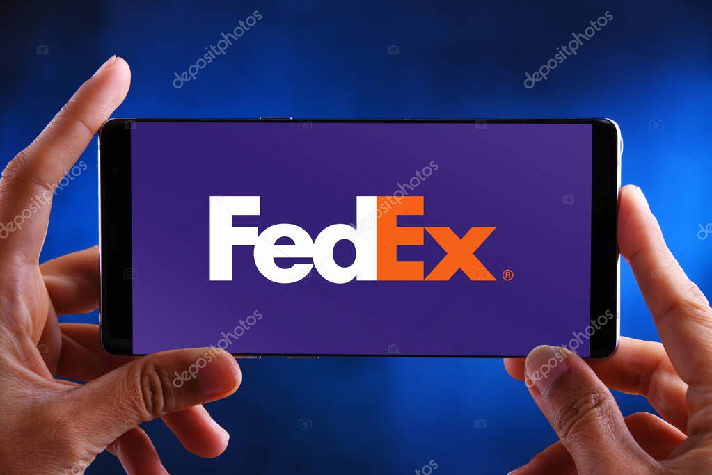 POZNAN, POL - JUL 10, 2019: Hands holding smartphone displaying logo of FedEx, an American multinational courier delivery services company headquartered in Memphis, Tennessee