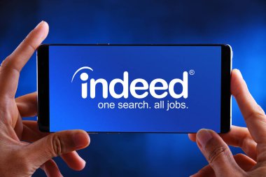 Hands holding smartphone displaying logo of Indeed clipart