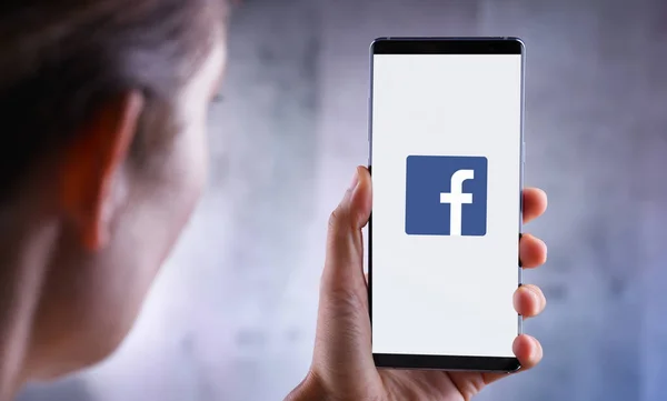 Wanita yang memegang smartphone menampilkan logo Facebook — Stok Foto