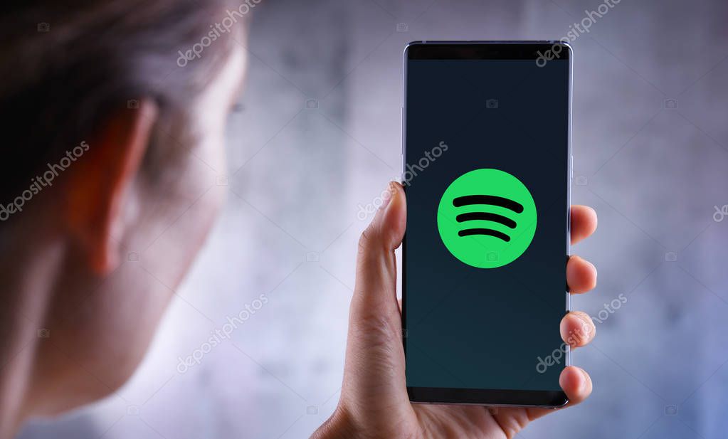 POZNAN, POL - JUL 10, 2019: Woman holding smartphone displaying logo of Spotify, a Swedish audio streaming platform that provides music and podcasts from record labels and media companies