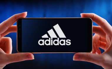 POZNAN, POL - 21 Mayıs 2020: Ayakkabı, giysi ve aksesuar tasarlayan ve üreten bir Alman şirketi olan Adidas 'ın akıllı telefon logosunu gösteren eller