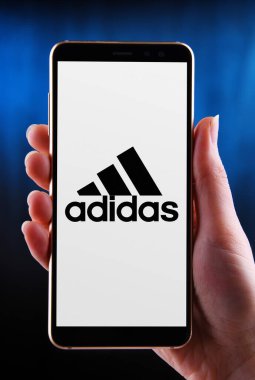 POZNAN, POL - 21 Mayıs 2020: Ayakkabı, giysi ve aksesuar tasarlayan ve üreten bir Alman şirketi olan Adidas 'ın akıllı telefon logosunu gösteren eller