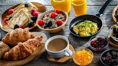 Kahvaltının yanında kahve, portakal suyu, kruvasan, mısır gevreği, çırpılmış yumurta ve krep var..