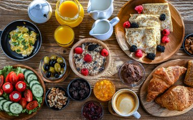 Kahvaltının yanında kahve, portakal suyu, kruvasan, mısır gevreği, çırpılmış yumurta ve krep var..