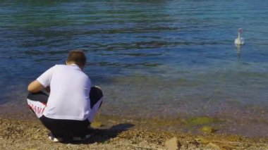 Sahilde oynayan genç çocuk ve suda yüzen kuğu. Güneşli bir günde seyahat tatil konsepti.