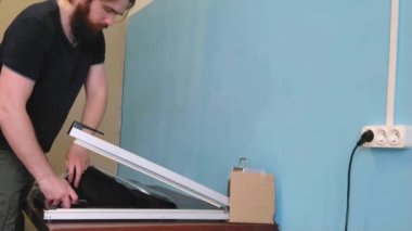 Adam tıbbi maske takan bir ceket fabrikasında çalışıyor. Özel teknolojiler kullanan tembel işçi asker plastik torbası. Çalışan koruma eldivenleri olmadan çalışır. İşçi koruma kurallarını ihlal eder..