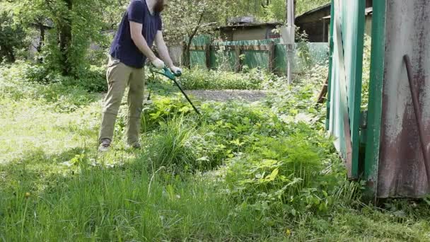 庭師は 生の草から庭で作業している間に電動トリマーをきれいにします 地方公共団体や民間労働者の夏の仕事 — ストック動画