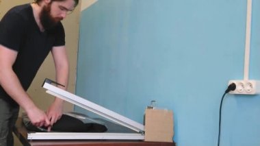 Adam tıbbi maske takan bir ceket fabrikasında çalışıyor. Özel teknolojiler kullanan tembel işçi asker plastik torbası. Çalışan koruma eldivenleri olmadan çalışır. İşçi koruma kurallarını ihlal eder..