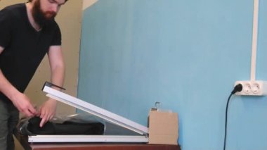 Adam tıbbi maske takan bir ceket fabrikasında çalışıyor. Özel teknolojiler kullanan tembel işçi asker plastik torbası. Çalışan koruma eldivenleri olmadan çalışır. İşçi koruma kurallarını ihlal eder..