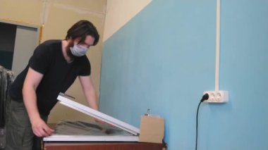 Adam tıbbi maske takan bir ceket fabrikasında çalışıyor. Özel teknolojiler kullanan tembel işçi asker plastik torbası. Çalışan koruma eldivenleri olmadan çalışır. İşçi koruma kurallarını ihlal eder..