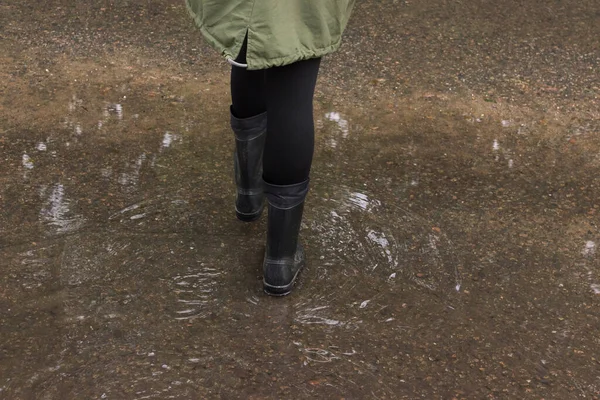 person stands in a puddle on a flooded street in rubber boots, close-up view of his feet. the rainy and monsoon season.The concept of children recreation, walks in any weather, the health of the child