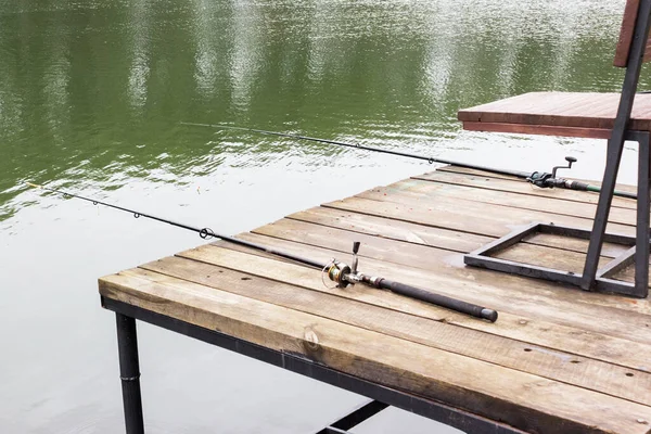 钓竿躺在水面上的一个木制码头上 旁边有一把椅子 渔民日的概念 户外运动和无趣运动的概念 — 图库照片