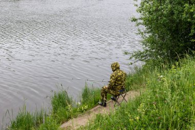 Kıyı şeridinde sandalyede oturan ve gölde balık tutan kişi. Bir adamın oltayı tuttuğu ve balık oltasıyla birlikte sudaki lezzetli balıkları yakaladığı arka plan görüntüsü. Uluslararası Balıkçılar Günü konsepti.