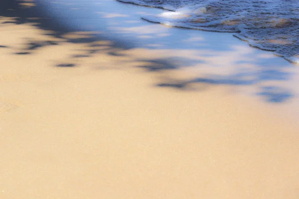 Foamy and crystal clear sea wave on the warm beach sand. Place for design and text. Concept for New Year\'s vacation abroad for holidays 2020-2021. This photo is a little out of focus