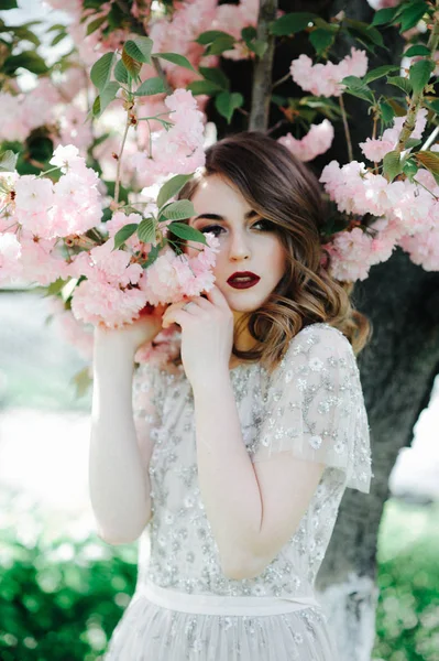非常に美しい少女を自然下で桜の木の近くのベール ベージュ結婚式ドレス花嫁を探して — ストック写真