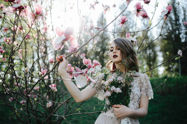 Very beautiful girl the bride under a veil, beige wedding dress near the tree Sakura is looking down, nature