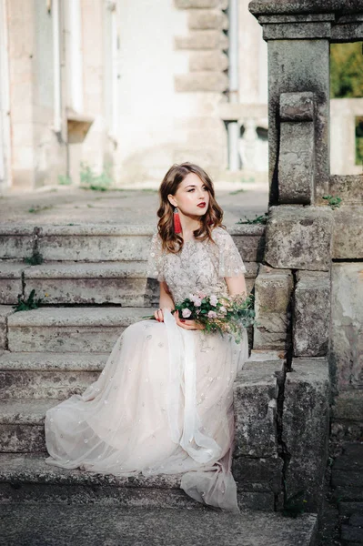 Bride.Young mannequin met perfecte huid en make-up, witte achtergrond. Mooie bruid op de trappen van de witte achtergrond. Een vrouw in een lange witte jurk zit op de trap. — Stockfoto