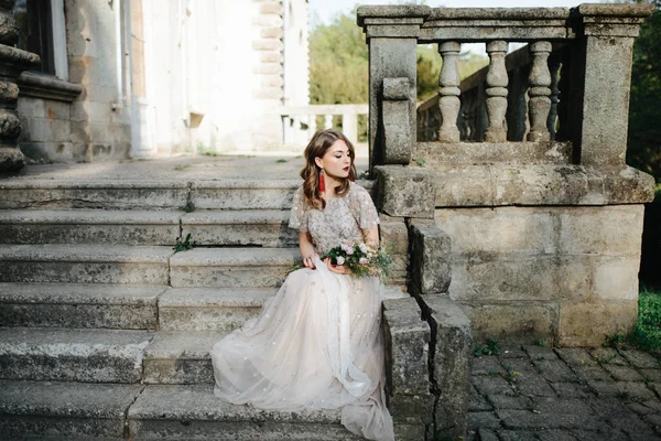 Bride.Young mannequin met perfecte huid en make-up, witte achtergrond. Mooie bruid op de trappen van de witte achtergrond. Een vrouw in een lange witte jurk zit op de trap. — Stockfoto