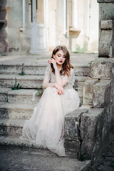 Bride.Young mannequin met perfecte huid en make-up, witte achtergrond. Mooie bruid op de trappen van de witte achtergrond. Een vrouw in een lange witte jurk zit op de trap. — Stockfoto