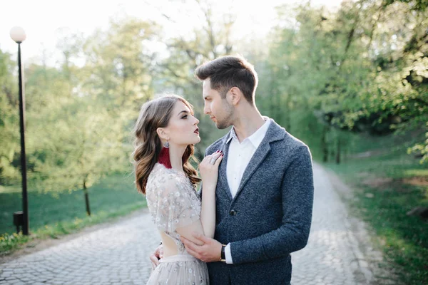 Pareja en traje de novia con un ramo de flores y vegetación está en las manos contra el telón de fondo del campo al atardecer, la novia y el novio —  Fotos de Stock