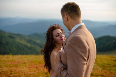 Birbirlerine aşık düğün çifti güzel manzarada kayaların yanında öpüşüyor ve sarılıyorlar.