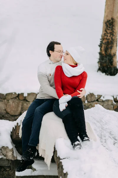 Um jovem casal de amantes em casacos de inverno e cachecóis sentados em um parque de neve — Fotografia de Stock