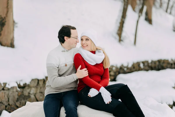 Una pareja de jóvenes amantes en chaquetas de invierno y bufandas sentados en un parque de nieve —  Fotos de Stock