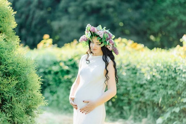 Young pregnant woman in spring lilac blooming garden. Romantic look with straw hat. Caucasian woman with long brown hairs. Concept of new life of nature and human. Waiting of baby