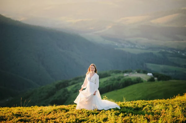 O femeie îmbrăcată într-o rochie de mireasă traversează câmpul spre munți — Fotografie, imagine de stoc